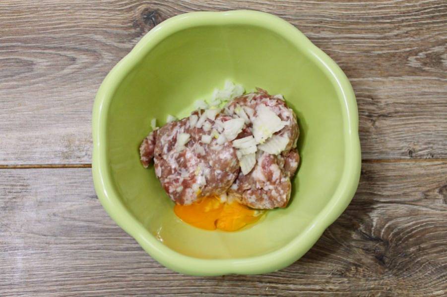 В миску выложите фарш, разбейте яйцо и добавьте мелко резанный репчатый лук.