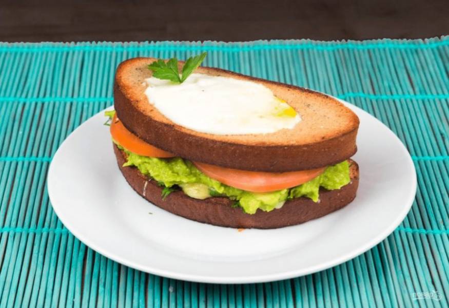 5. Затем соберите сэндвич: на ломтик с сыром намажьте авокадо и добавьте нарезанный пластинками помидор. Прикройте ломтиком с яичницей. Приятного аппетита!