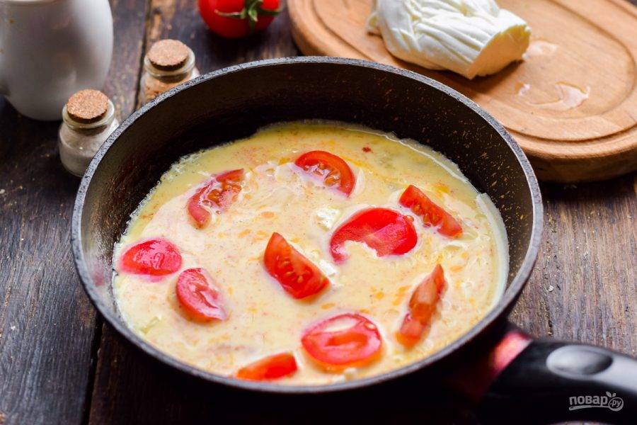 Сковороду смажьте маслом, влейте омлетную смесь с сыром, добавьте нарезанные дольками помидоры. Готовьте омлет под крышкой 7-8 минут.