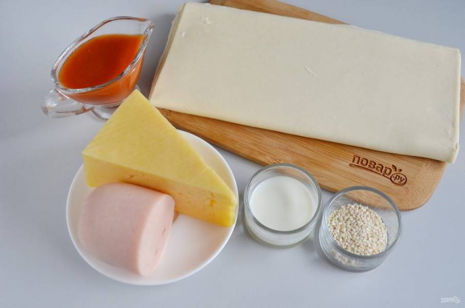 Тесто разморозьте при комнатной температуре. Натрите на крупной терке сыр и ветчину. Включите духовку прогреваться на 220 градусов.