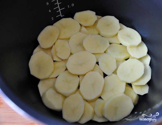 Картошечку вымойте и очистите от кожуры. Затем нарежьте ее на тонкие кружочки. Это удобно делать специальным слайсером или насадкой на терке. Чашу мультиварки смажьте растительным маслом, выложите в нее половину картофеля.