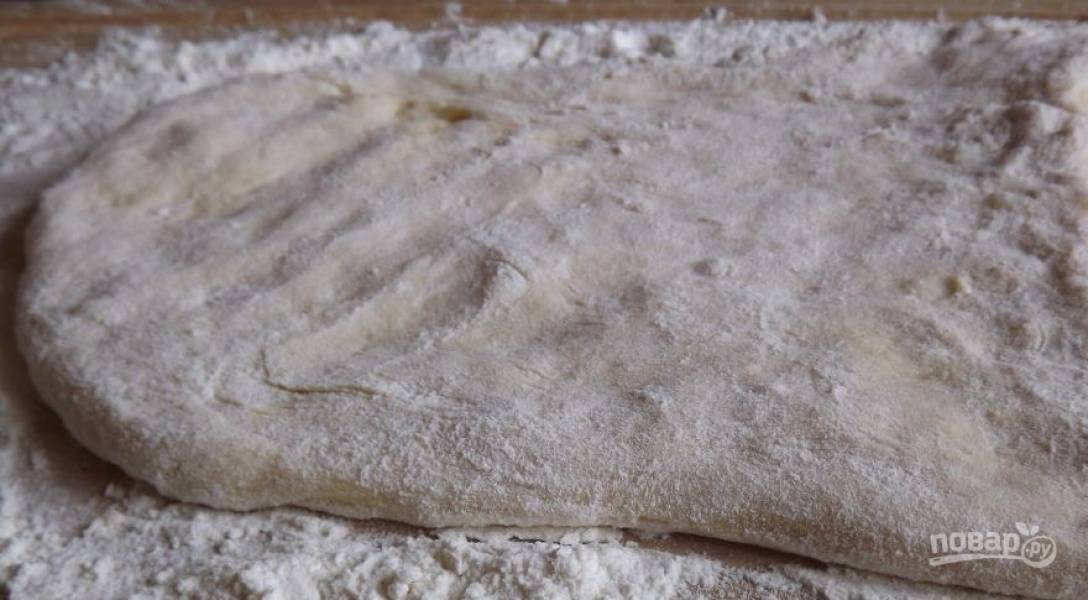 Присыпьте рабочую поверхность мукой и выложите на нее подошедшее тесто. Затем раскатайте тесто в пласт толщиной около одного сантиметра, посыпая его мукой, чтобы тесто не липло к рукам и скалке. 