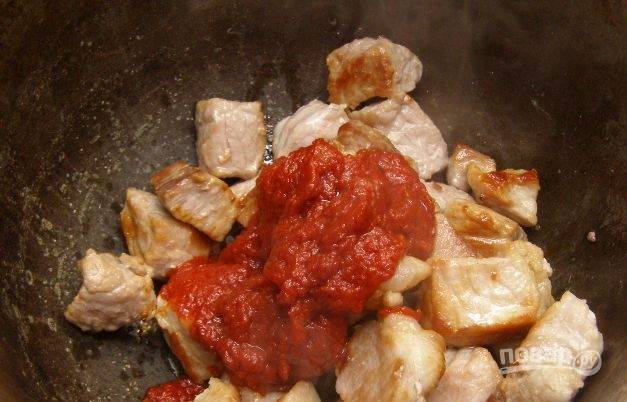 Переложите обжаренное мясо в кастрюльку с толстым дном или в казанок. Добавьте к мясу томатную пасту. 