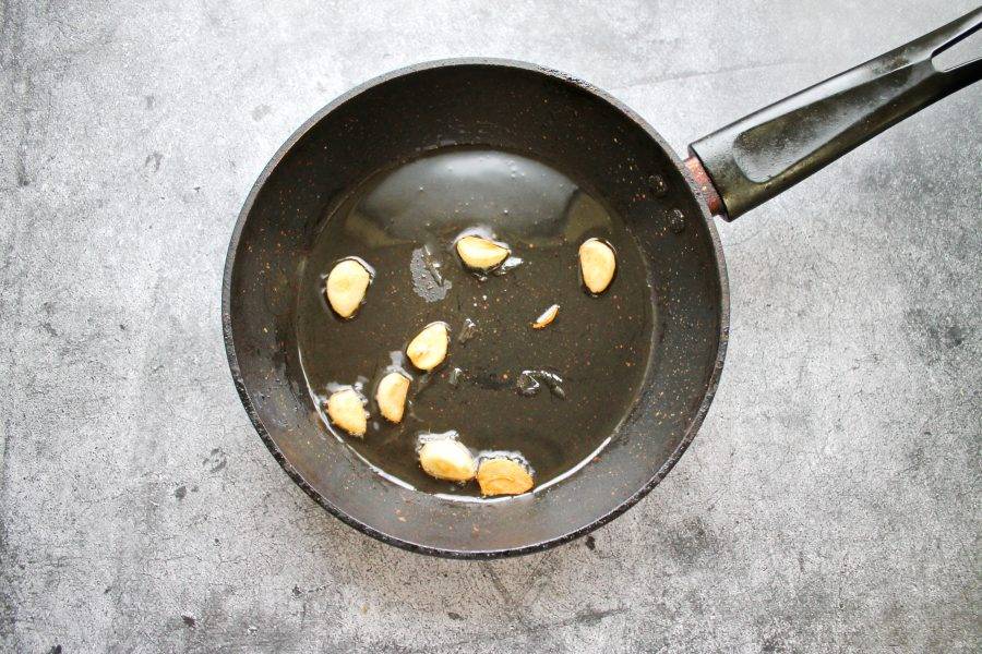В сковороду налейте растительное масло и разогрейте на среднем огне. Дольки чеснока очистите, разрежьте пополам и выложите в масло. Обжаривайте их до золотистого цвета и удалите.
