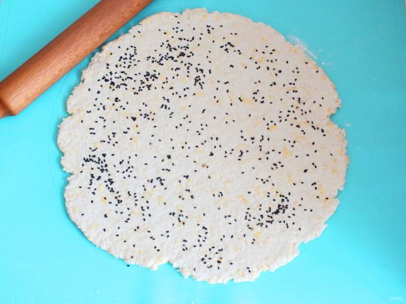 На рабочей поверхности раскатайте тесто. Посыпьте сверху семенами кунжута, слегка прокатайте скалкой.