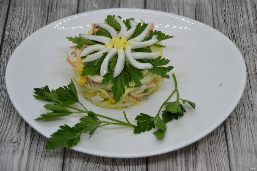 Чтобы придать салату наиболее привлекательный и праздничный вид, оформите сверху украшение в виде "ромашки", из той половинки яйца, которую оставили при нарезке, положите пару веточек зелени. Салат готов. Приятного аппетита!