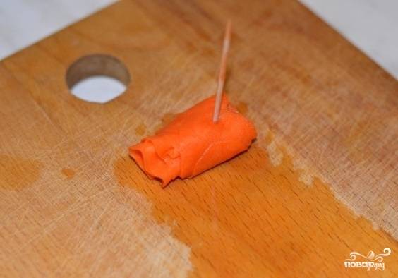 Сырую морковку очищаем от кожуры. Нарезаем тончайшими кружочками. Их можно сделать при помощи комбайна. Опускаем в соленую воду на пару минут. Обсушиваем и скрепляем зубочисткой в красивую розочку.