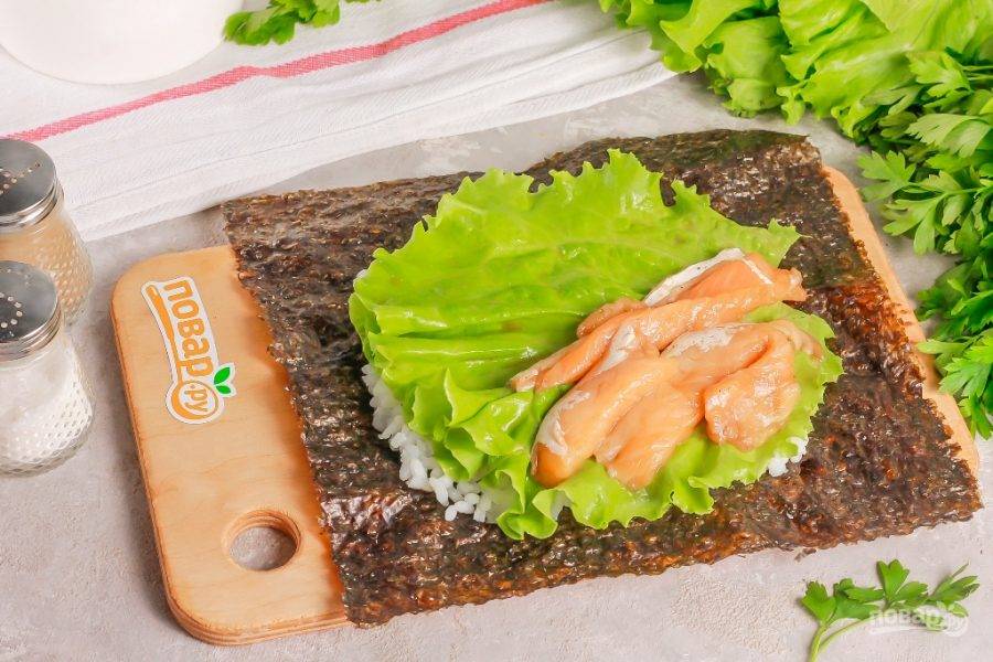 Обмажьте рис сливочным сыром. Промойте листья салата и выложите сверху. На половину рисового слоя выложите ломтики копченого лосося.