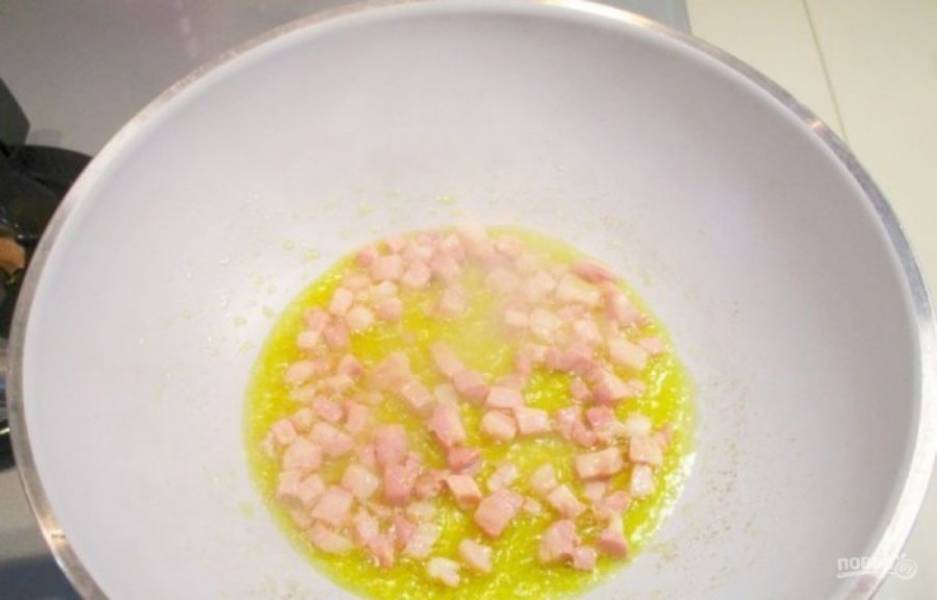 Разогрейте в глубокой сковороде немного оливкового масла  (можно приправить зубчиком чеснока), затем добавьте нарезанный кубиками бекон и обжарьте.