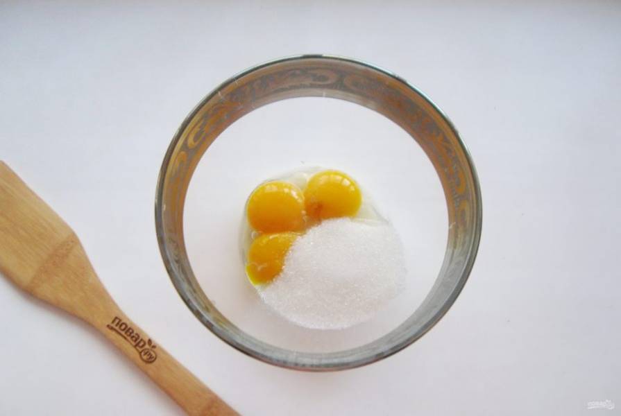 Отделите желтки от белков у четырех яиц и выложите в миску. Добавьте сахар.