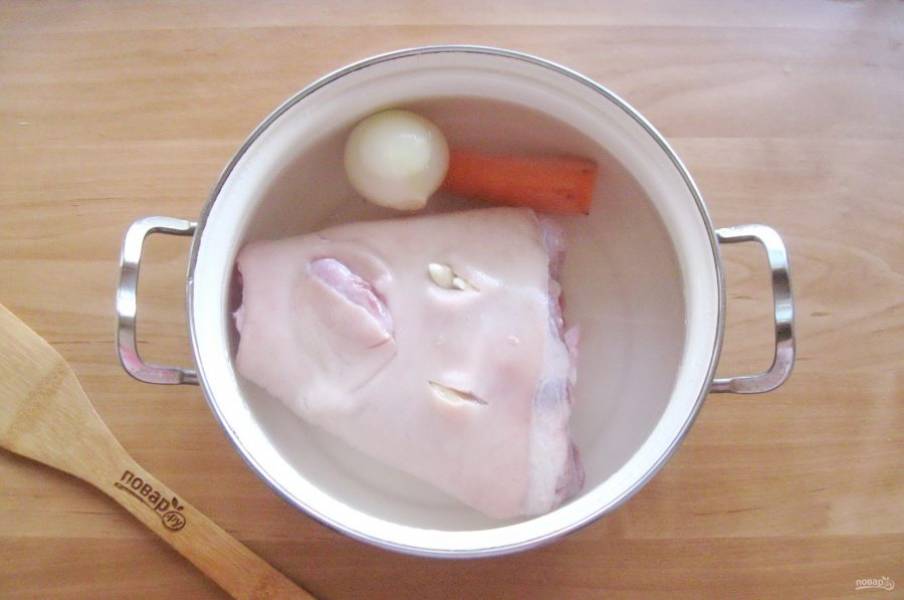 Выложите рульку в кастрюлю и залейте водой, чтобы она накрывала мясо полностью. Добавьте лук и морковь. Овощи предварительно очистите и помойте.
