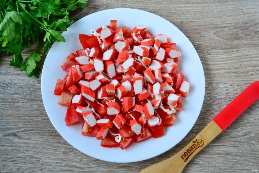 На плоскую тарелку выложите помидоры, слегка присолите их. Затем выложите крабовые палочки. 