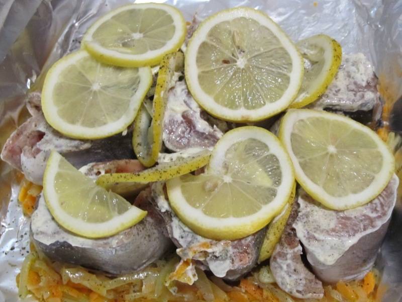 На овощи выкладываем срезом вниз горбушу, смазываем рыбу майонезом и раскладываем на нее ломтики лимона. 