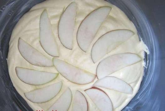 Яблоко помойте и нарежьте на дольки. Половину выложите на тесто. Потом залейте вторым слоем и ещё раз разложите дольки. В конце залейте оставшееся тесто.