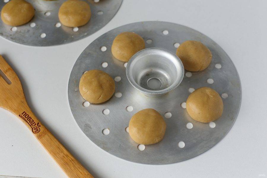 Отщипывайте от теста кусочки и формируйте шарики, размером чуть больше грецкого ореха. Все заготовки выложите на некотором расстоянии друг от друга на смазанную маслом решетку пароварки.
