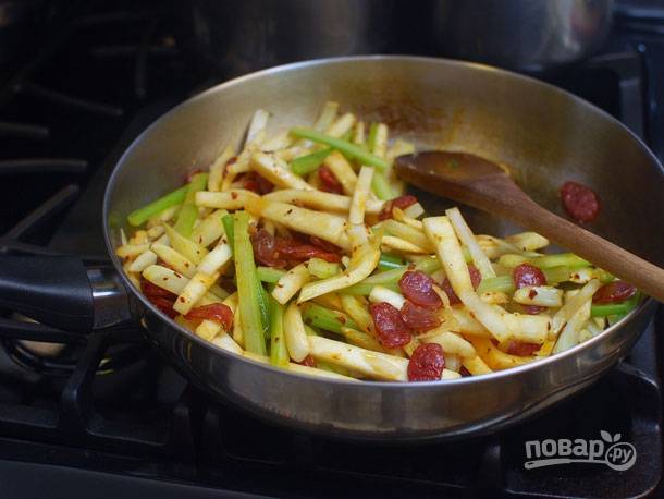 7. Верните на сковороду колбаски, добавьте соевый и острый соус. Перемешайте и уже через минуту жареный корень сельдерея с колбасками готов.
