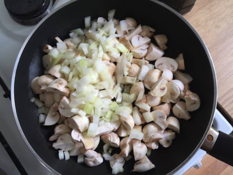 3. Затем очистите луковицу, нарежьте её некрупными произвольными кусочками. На сковороду налейте растительное масло, выложите лук и грибы. Обжарьте овощи до лёгкого золотистого цвета.