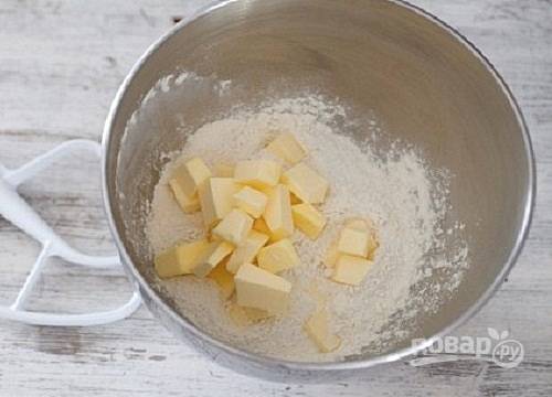 Просеиваем в миску муку и добавляем охлажденное сливочное масло, нарезанное кубиками. Активными движениями перетираем в крошку.