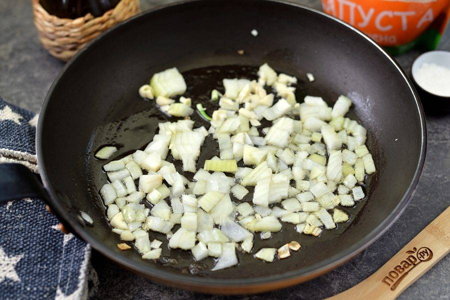 Нарежьте лук мелким кубиком, порубите чеснок, переложите их в разогретое растительное масло на сковороде. Обжарьте минуты 2 на умеренном огне. 