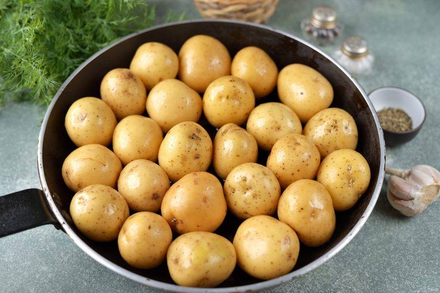 Переложите картофель в большой противень, он должен лежать в один ряд. Если у вас есть сковорода с железной ручкой — она идеально подходить для приготовления этого блюда. Сбрызните картофель оливковым маслом, тщательно обваляйте в нем каждую картофелину. Отправьте форму с картошкой в предварительно разогретую до 200 градусов духовку минут на 20. 