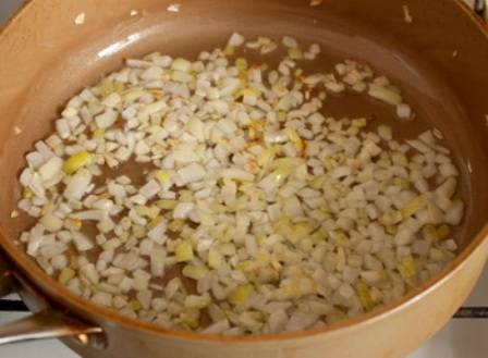 Для начала мы наливаем в сотейник растительное масло и ставим его на огонь. Когда масло нагреется, выкладываем в него нарезанный мелко репчатый лук и измельченный чеснок, жарим овощи до золотистого цвета.