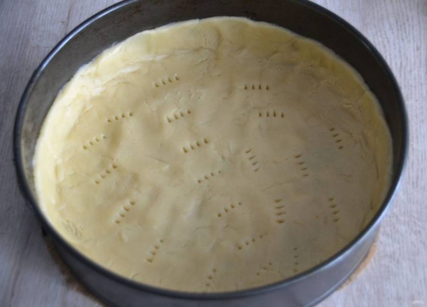 Выложите тесто в разъемную форму (диаметром 26 см.), распределите по форме, сформируйте бортики высотой около 2 см., сделайте проколы вилкой.