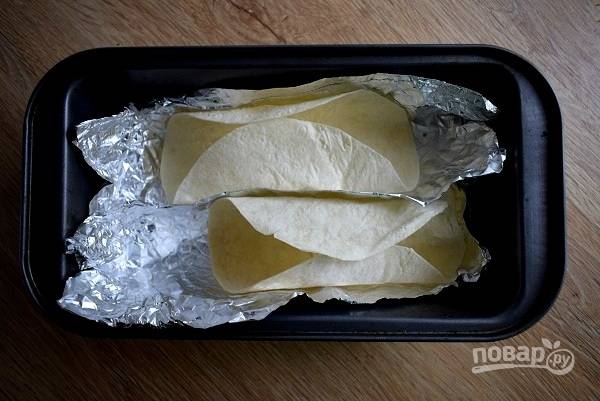 Лепешки тортилья сверните пополам, зафиксируйте с помощью фольги и запекайте в духовке в течение 3-4 минут при 180 °C.