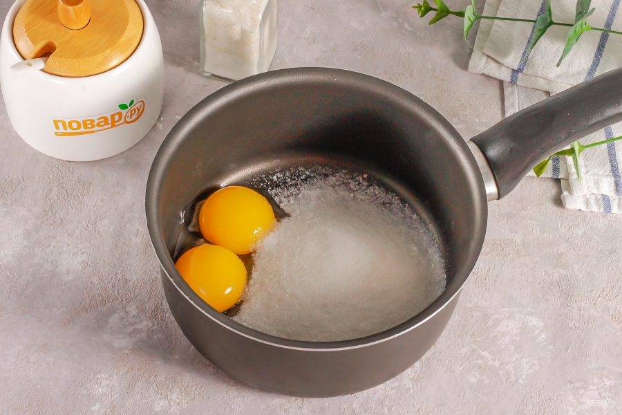 Всыпьте в ковш или кастрюлю с антипригарным дном сахар и выложите желтки куриных яиц. Белки вам не потребуются в рецепте, можете приготовить из них другое блюдо.