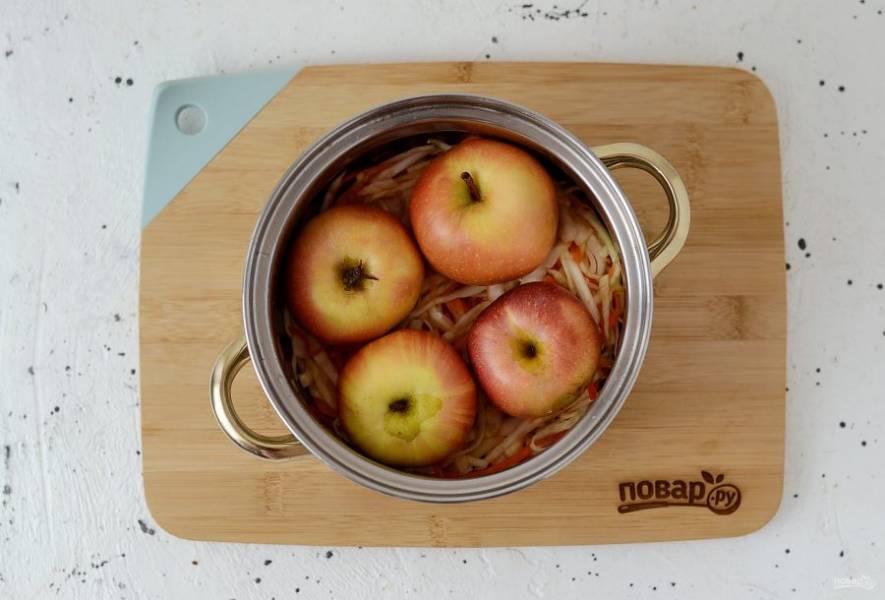 Выложите на дно кастрюли часть капусты, плотно примните руками. Сверху выложите яблоки.