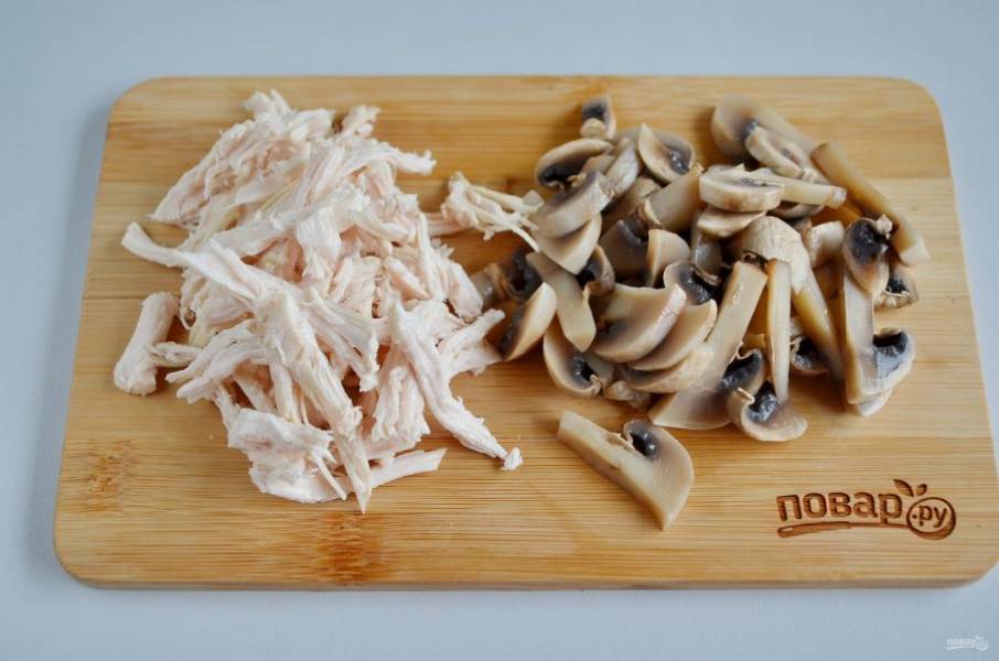 Остывшее мясо разберите на волокна. Вареные грибы порежьте на половинки, потом слайсами.