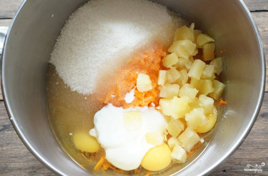 Влейте растительное масло и йогурт, добавьте сахар и порезанные кусочками ананасы. Тщательно перемешайте.