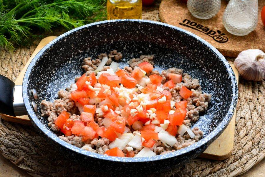 Помидоры нарежьте кубиками и также добавьте к фаршу. Добавьте мелко нарезанный чеснок. Все перемешайте и жарьте пару-тройку минут.