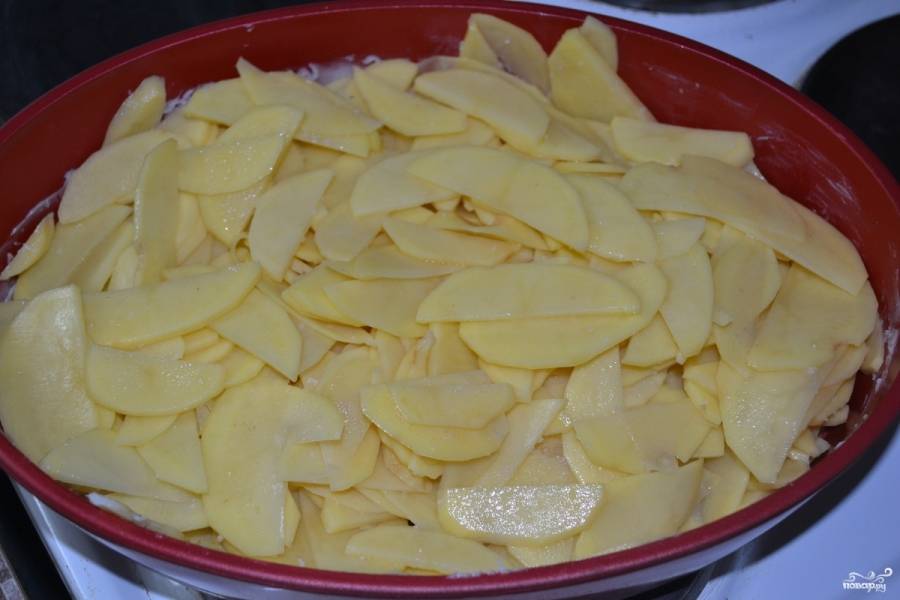 Лук порежьте кубиками и посолите.
Потом выложите овощи в форму. На дно положите слой картофеля, а затем чередуйте с луком слоями. Полейте картошку с луком половиной сметаны.
