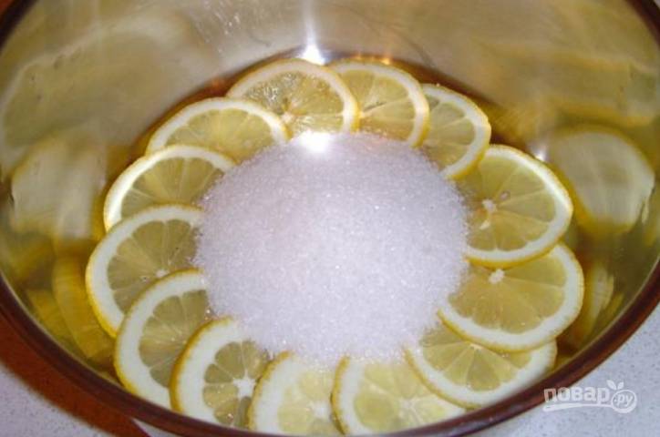 Лимоны промойте, один нарежьте тонкими колечками. Переложите в кастрюльку и засыпьте сахаром (100 грамм). Влейте 100 мл воды. Варите на медленном огне 10 минут.