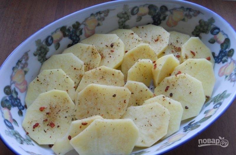В форму для выпечки влейте масло. Картофель почистите, промойте и нарежьте кружками. Выложите их в форму. Добавьте соль и специи.