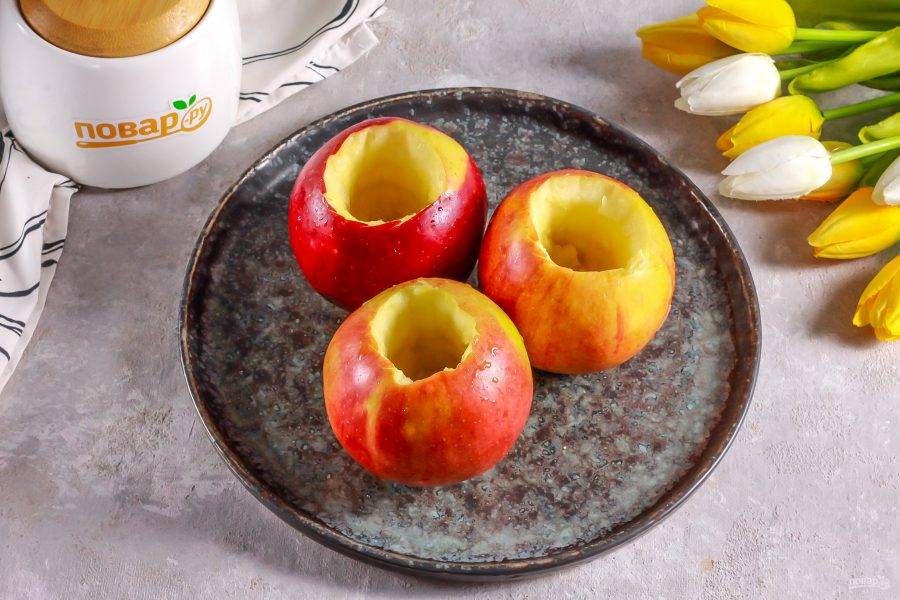 Яблоки промойте в воде, аккуратно вырежьте сверху каждого плода отверстие и удалите семенные блоки, стараясь не прорезать плод до низа.