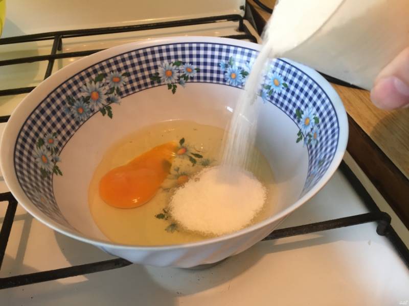 В отдельную посуду разбейте 2 яйца. Туда же засыпьте стакан сахарного песка. Хорошо взбейте смесь вилкой или блендером и оставьте сахар растворяться.