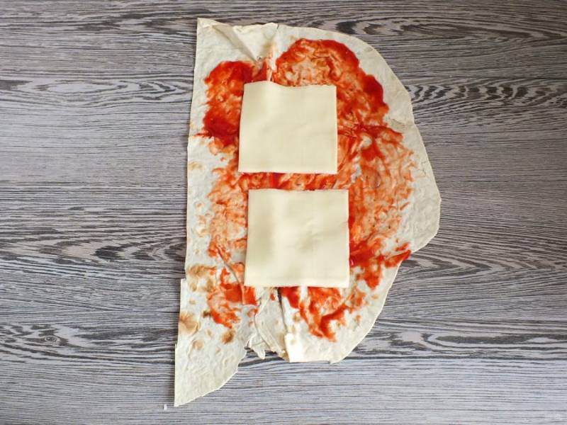 Возьмите одну полосу из лаваша. Смажьте кетчупом, выложите по две пластинки сыра.