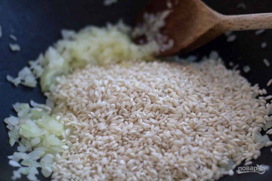 В другой сковороде на разогретом масле обжарьте измельчённый лук до мягкости. Потом к нему добавьте рис для ризотто. Обжарьте ингредиенты, помешивая, до мягкости риса.