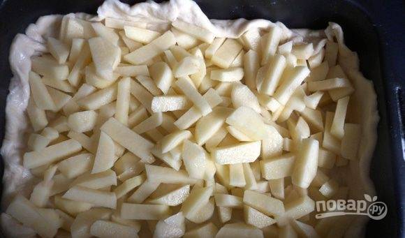 Форму для выпечки смажьте маслом. Большую часть теста раскатайте. Уложите на дно формы, сделав бортики. Сверху выложите нарезанный и очищенный картофель. Подсолите его.