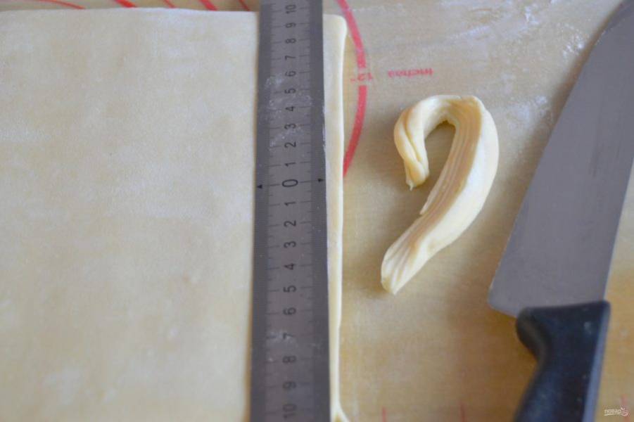 Для окончательной формовки круассанов, слегка подпылите мукой рабочую поверхность стола.  Раскатайте тесто таким образом, чтобы "ключ" был сбоку, на длину примерно 30 см. Каждый раз, после холодильника аккуратно продавливайте тесто скалкой, чтобы оно было более пластичным. Чтобы слои при выпечке раскрылись, подрежьте ножом неровные края теста. Сделайте разметку теста по краям. Нарежьте тесто на треугольники по линейке, соединив метки.