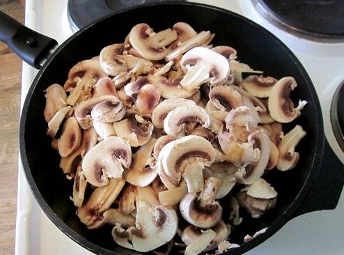 Итак, начнем с того, что промоем грибы и нарежем их тонкими пластинками. Выкладываем шампиньоны в разогретую сковородку, доливаем к ним немного водички и тушим грибы на медленном огне в течение 25-30 минут.