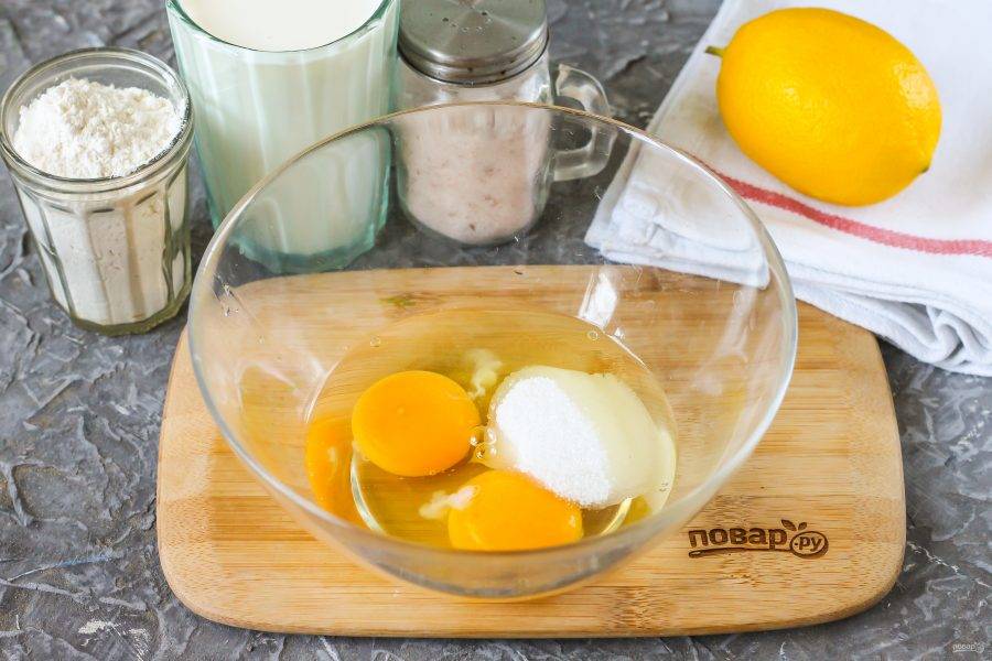 Вбейте куриные яйца в глубокую емкость, всыпьте сахар. Так как в тесто будет вводиться лимонный сок, то чуть увеличьте норму сахарного песка, чтобы блины не получились кислыми на вкус.
