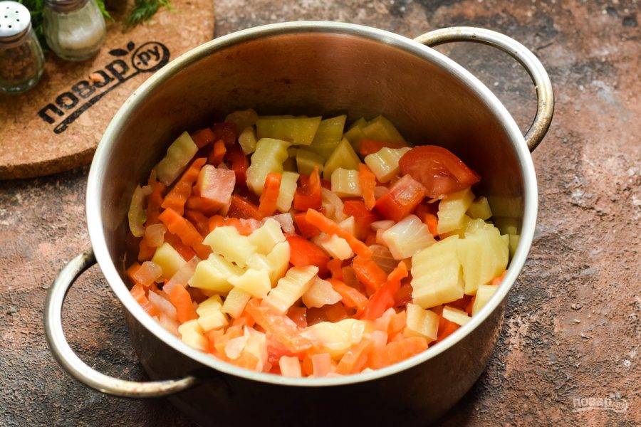 В кастрюле разогрейте растительное масло, выложите лук, морковь, перец, жарьте 3 минуты, после добавьте томаты и картофель, готовьте еще 2-3 минуты.