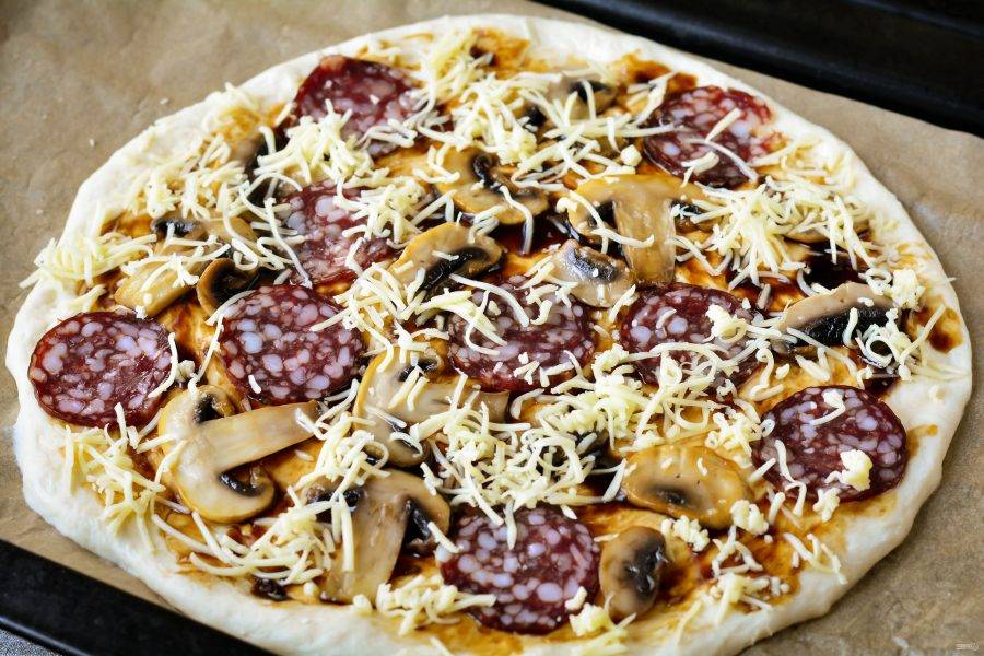 Присыпьте тертым сыром и поставьте пиццу в разогретую до 200 градусов духовку.