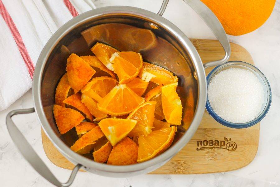 Ошпарьте цитрусовые кипятком и снимите цедру с апельсина — она может горчить. Используйте ее в других рецептах. Затем разрежьте плод на четыре части и удалите косточки, если они там присутствуют. Нарежьте ломтиками и выложите нарезку в кастрюлю.