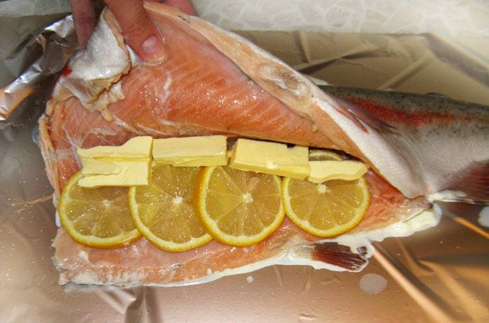 Теперь мы выкладываем ломтики лимона внутрь рыбы, добавляем небольшие кусочки сливочного масла, чтобы форель не вышла сухой. 