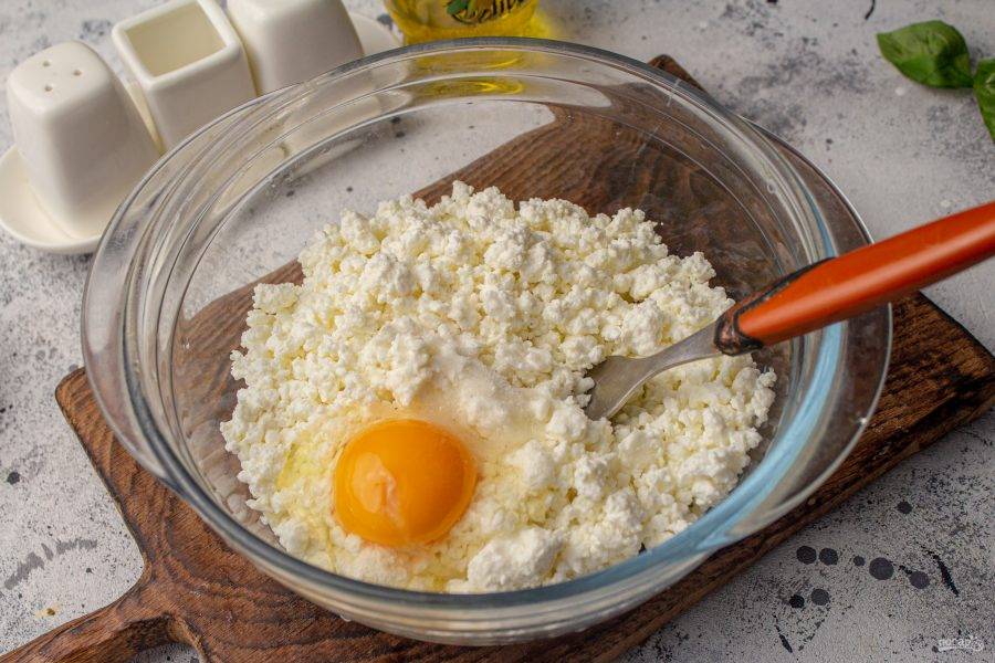 В подходящую посуду выложите творог, добавьте соль по вкусу и вбейте яйцо. Перемешайте творог с яйцом.  