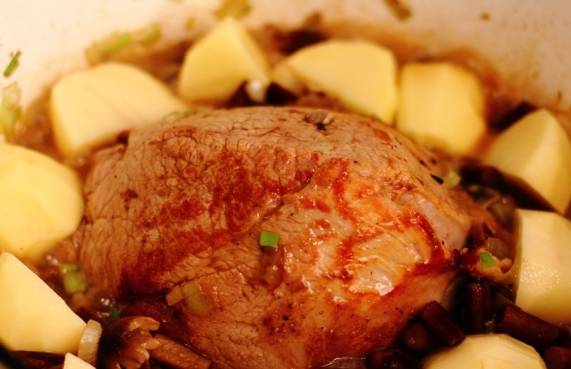 По бокам от мяса раскладываем очищенный и нарезанный крупными кусками картофель. Ставим посуду в разогретую до 180 градусов духовку и готовим жаркое в течение часа. 