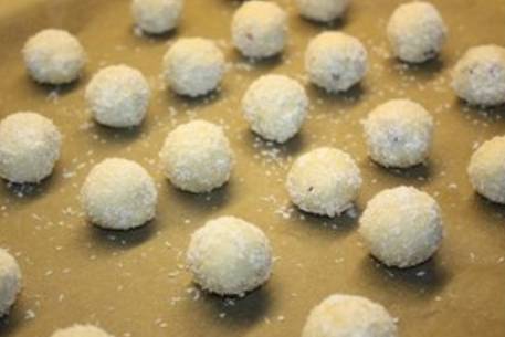 Сформируйте таким образом печенье-шарики, обваляйте его в кокосовой стружке и выложите на противень, застеленный бумагой для выпечки.